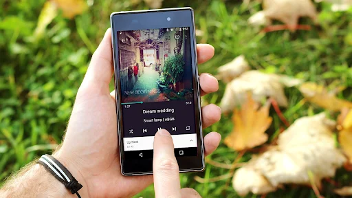 Hand holding phone with Fuel Music Player app showing now playing screen with album art and playback controls