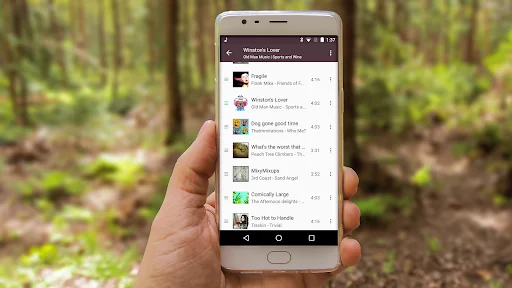 Hand holding smartphone displaying Fuel Music Player playlist with song titles and album covers in list view